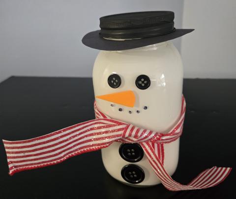 Jar Snowman picture of snowman made from a mason jar with black buttons, carrot nose, black hat and red and white scarf