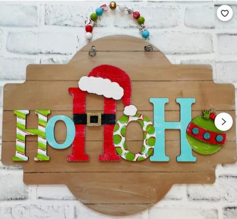 A wooden sign which spells out HoHoHo with the middle H having a Santa hat and the last O being an ornament